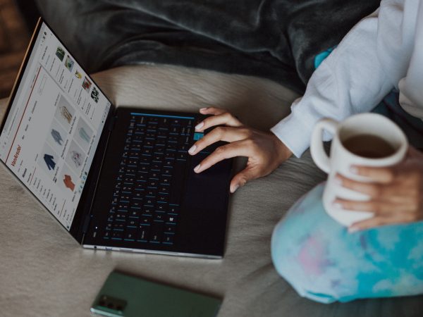 Person holding a cup of coffee while working on a laptop computer